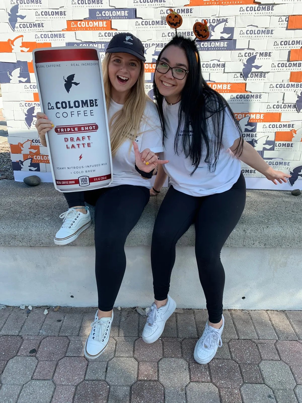 Two La Colombe campus brand ambassadors posing in front of the handmade recycled box backdrop at a sampling event