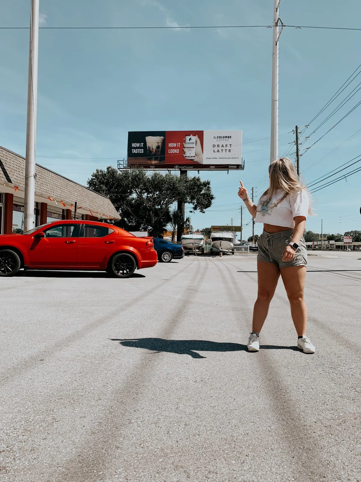 Blue Sitten pointing up at a La Colombe Draft Latte billboard reading How It Tastes, How It Looks in a Florida parking lot