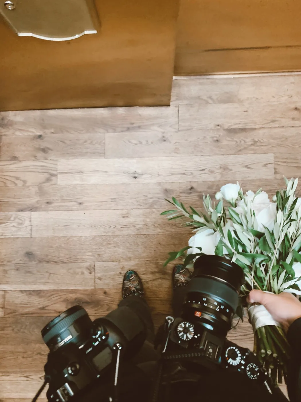 Overhead of two cameras and a bouquet on a wood floor at a shoot
