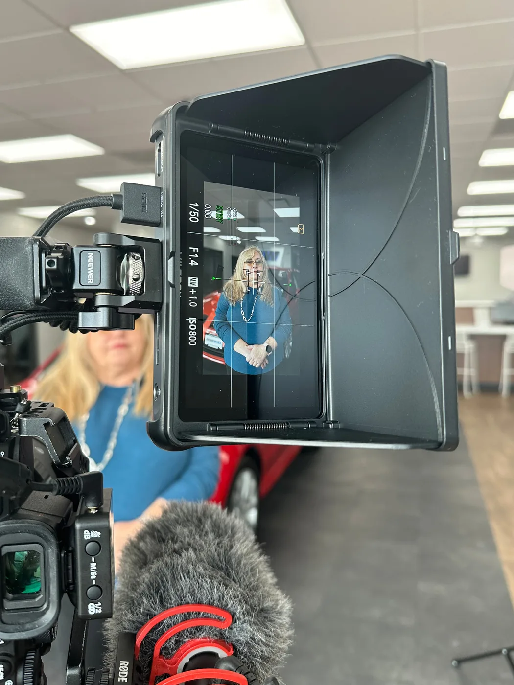 Camera monitor framing a dealership interview beside a red car