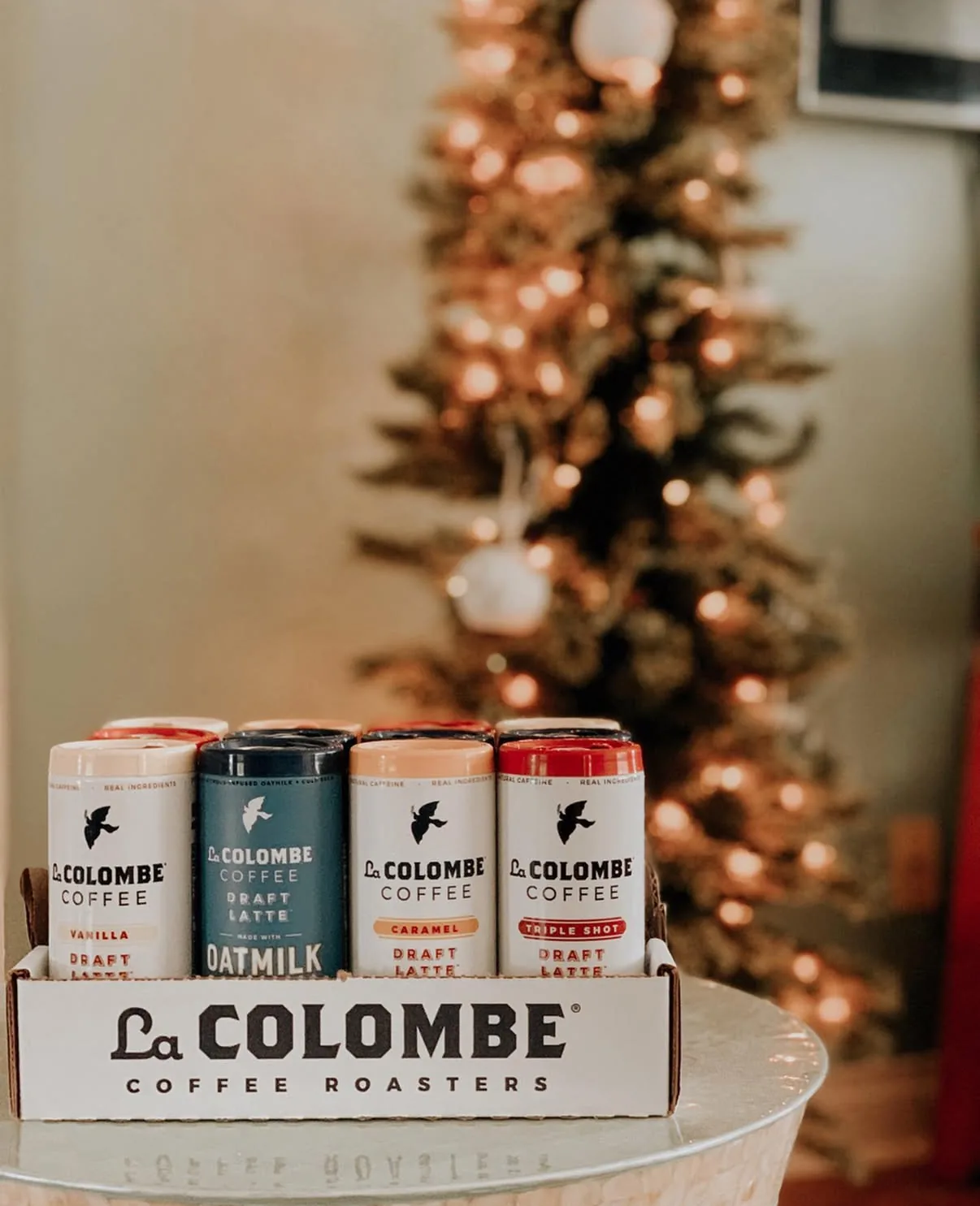 Four Draft Latte flavors in a La Colombe Coffee Roasters shipping tray in front of a lit Christmas tree