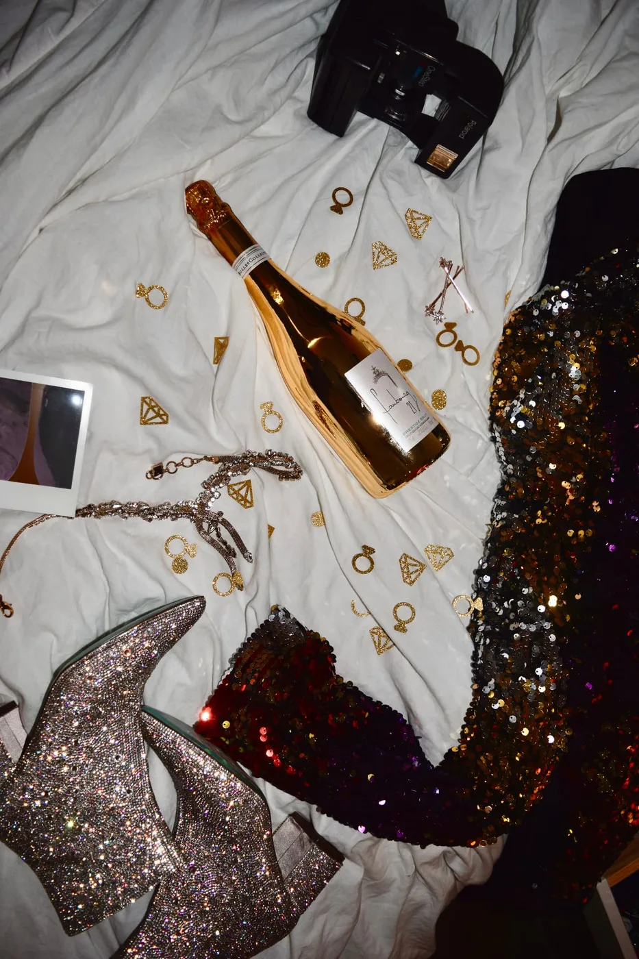 Styled flat lay of sequins, champagne, and a Polaroid camera